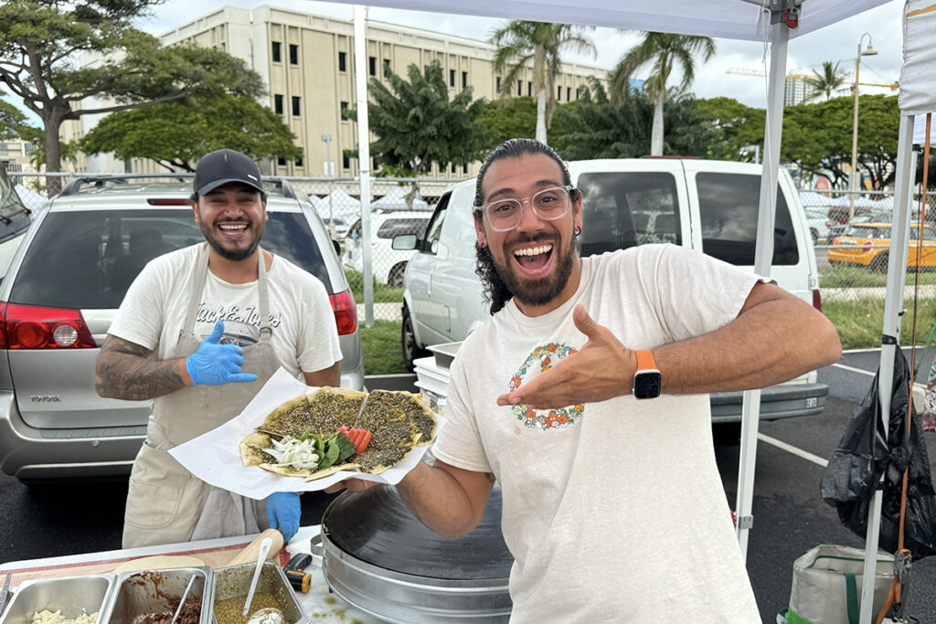 two smiling men hold up a grilled flatbread